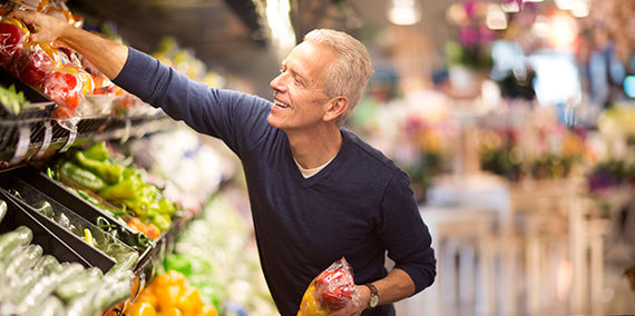 A senior man selects vegetables at a grocery store