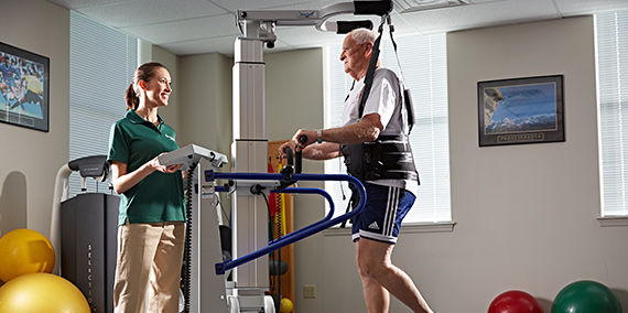 An older man is guided through light gate therapy on a treadmill