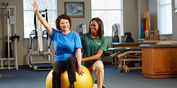 A woman uses an exercise ball alongside her physical therapist